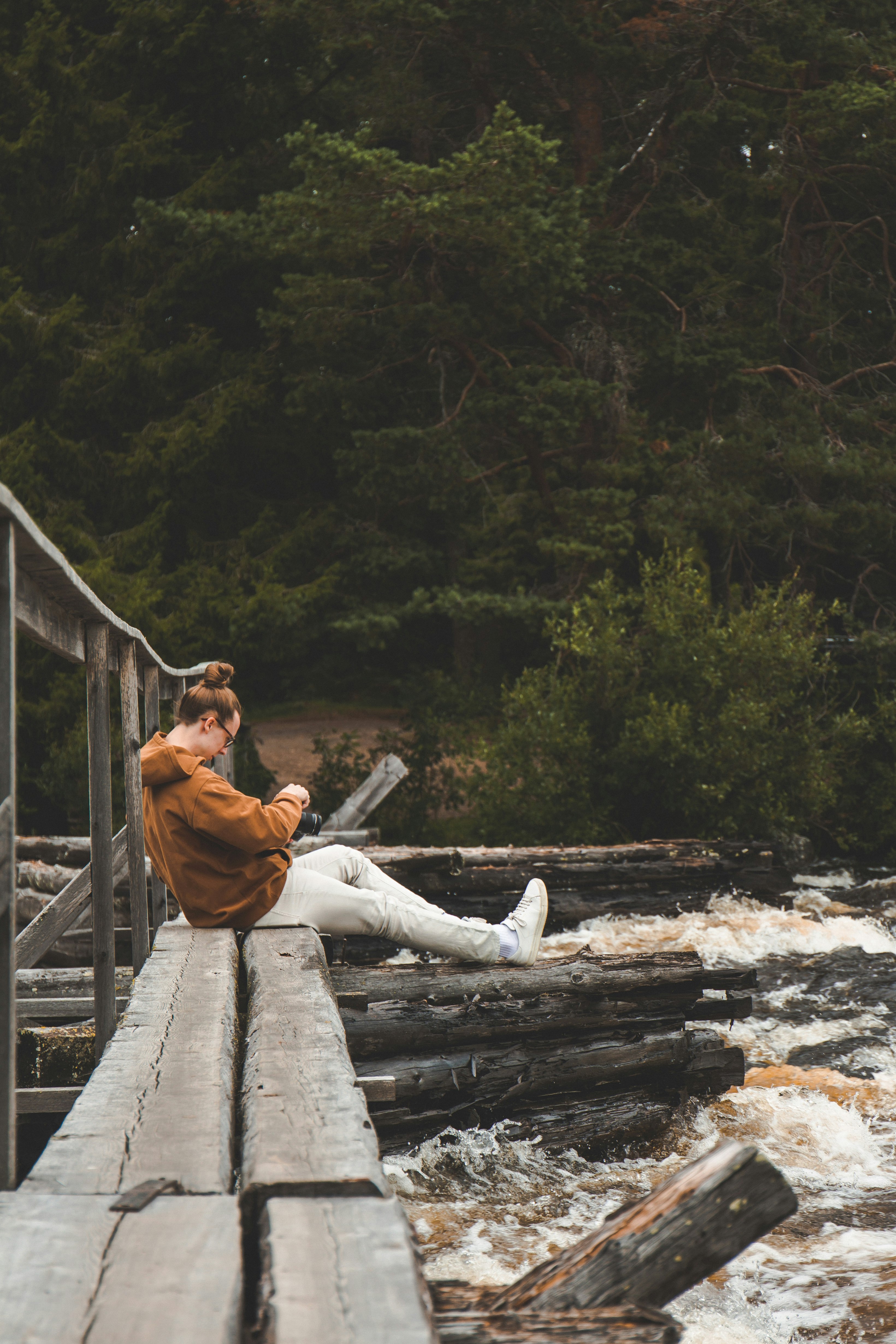 man in brown jacket sitting on brown wooden bridge during daytime